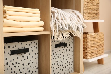 Photo of Folded linens and boxes on shelving unit indoors. Home textile storage