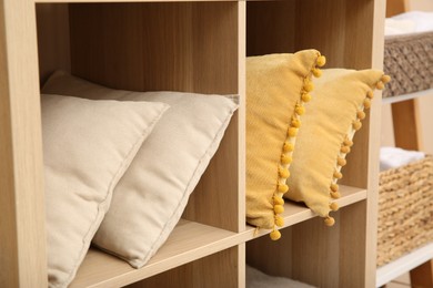 Photo of Clean pillows on shelving unit indoors. Home textile storage