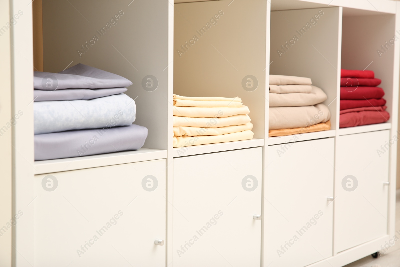 Photo of Folded bedsheets on shelving unit indoors. Home textile storage