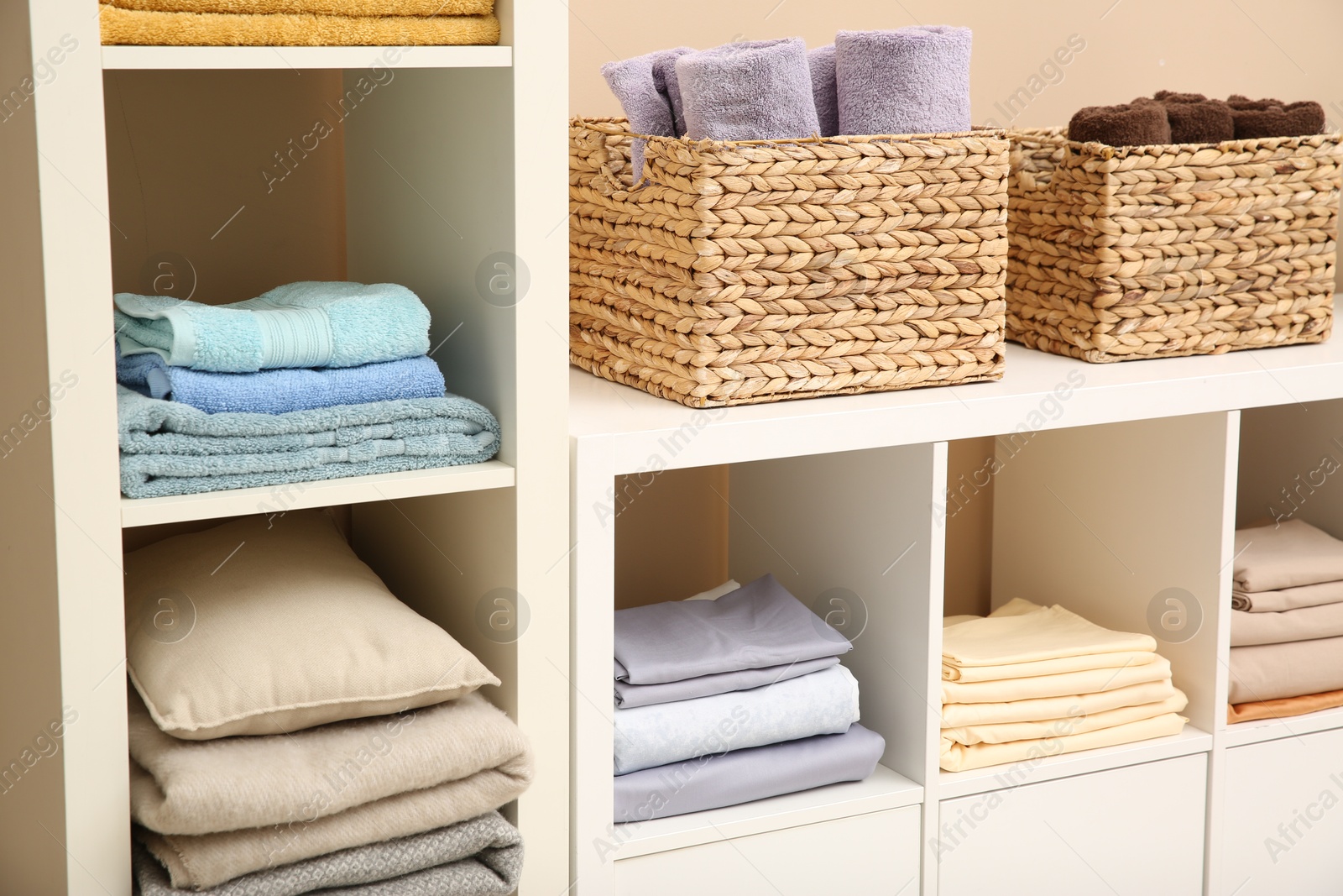 Photo of Folded linens, towels and pillow on shelving unit indoors. Home textile storage