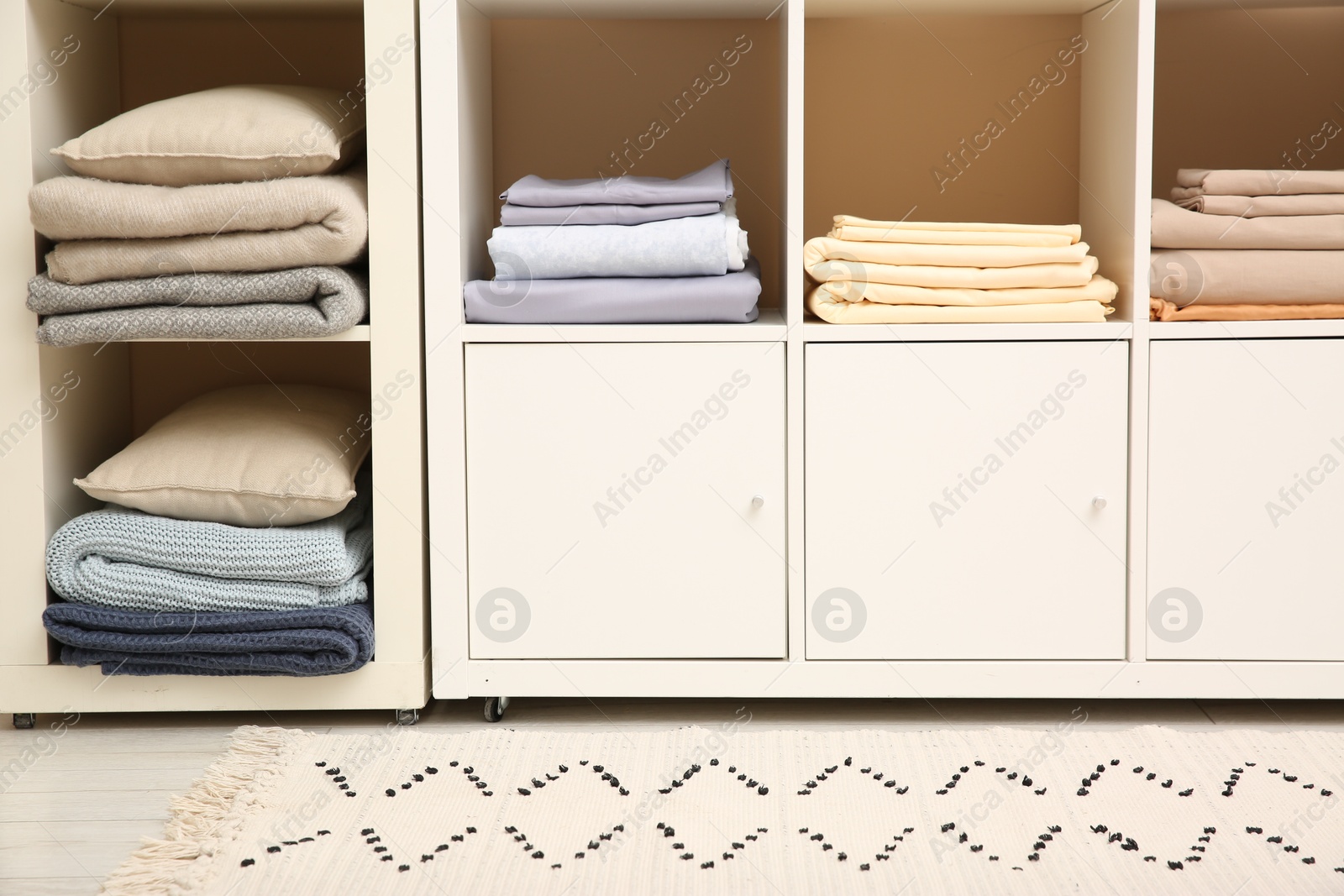 Photo of Folded linens and pillows on shelving unit indoors. Home textile storage