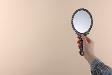 Photo of Woman holding beautiful mirror on beige background, closeup. Space for text