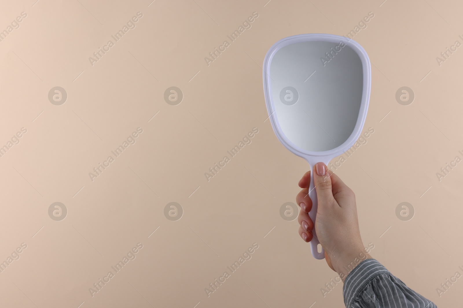 Photo of Woman holding handheld mirror on beige background, closeup. Space for text