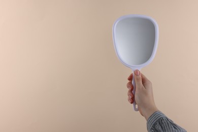 Woman holding handheld mirror on beige background, closeup. Space for text