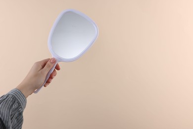 Photo of Woman holding handheld mirror on beige background, closeup. Space for text