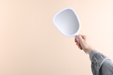 Woman holding handheld mirror on beige background, closeup. Space for text