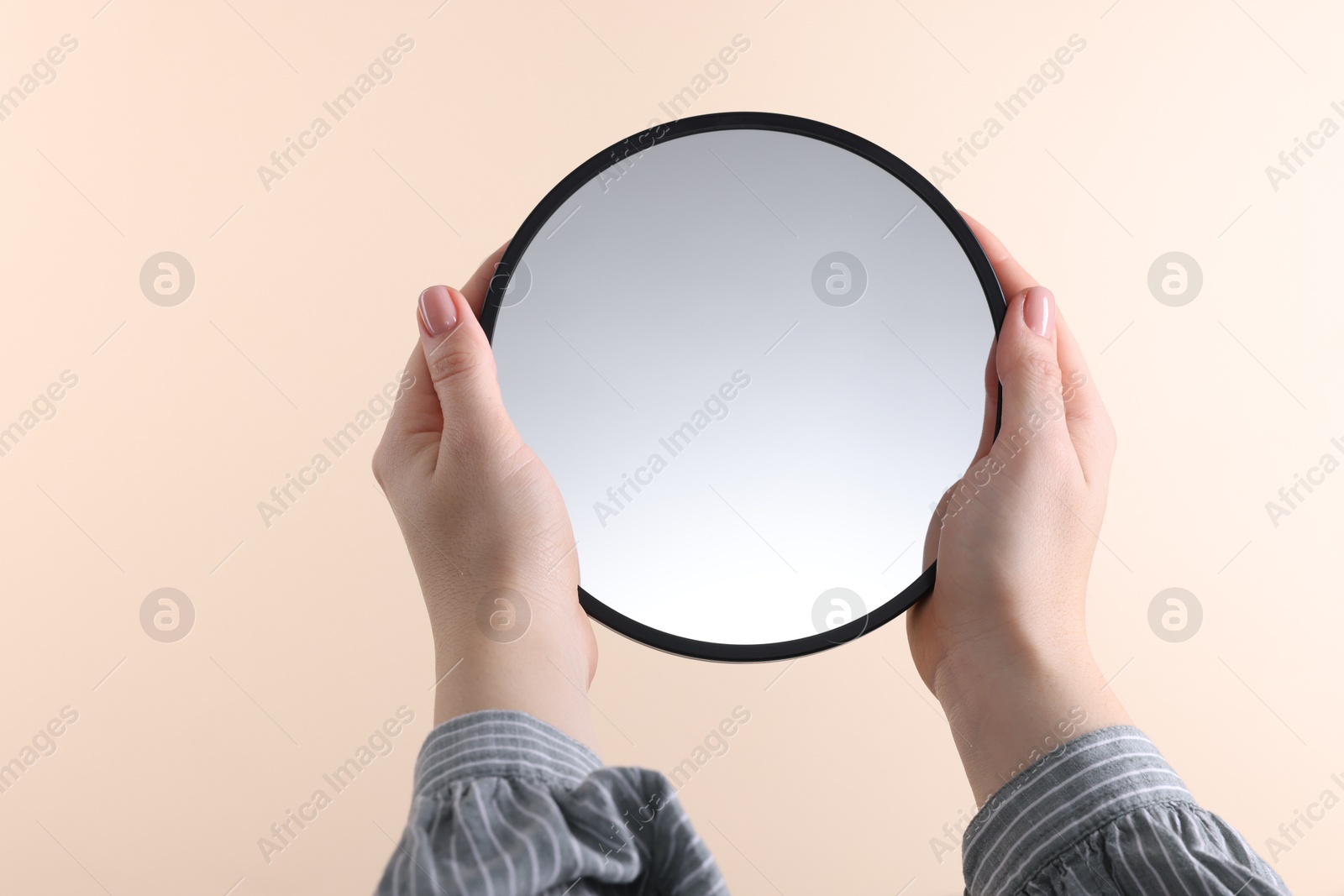 Photo of Woman holding round mirror on beige background, closeup