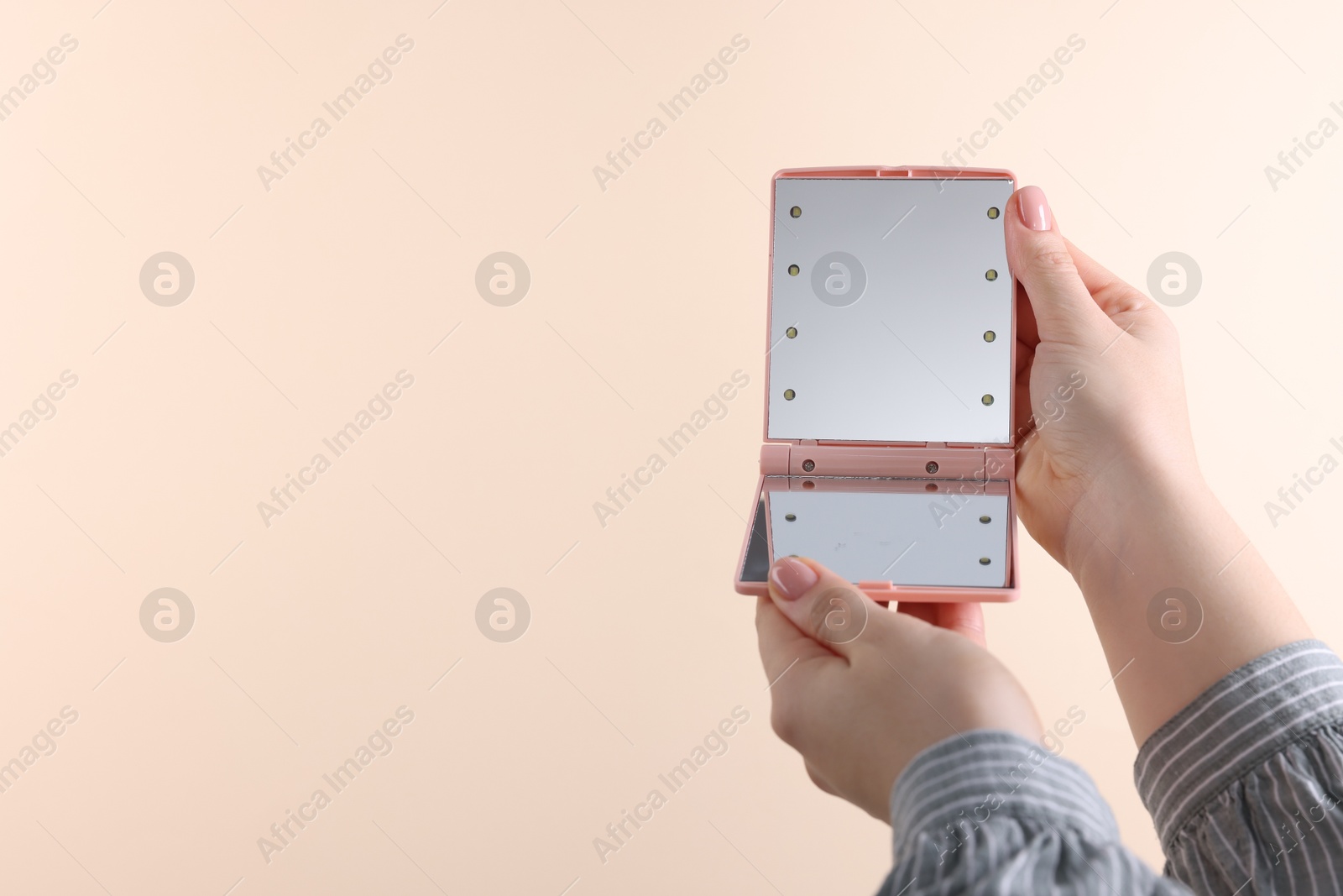 Photo of Woman holding pocket mirror on beige background, closeup. Space for text