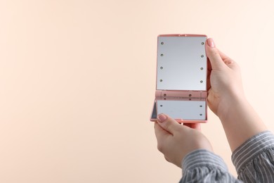 Photo of Woman holding pocket mirror on beige background, closeup. Space for text