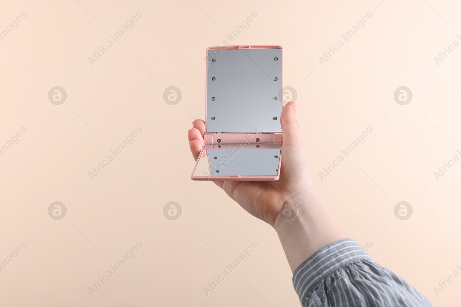 Photo of Woman holding pocket mirror on beige background, closeup. Space for text