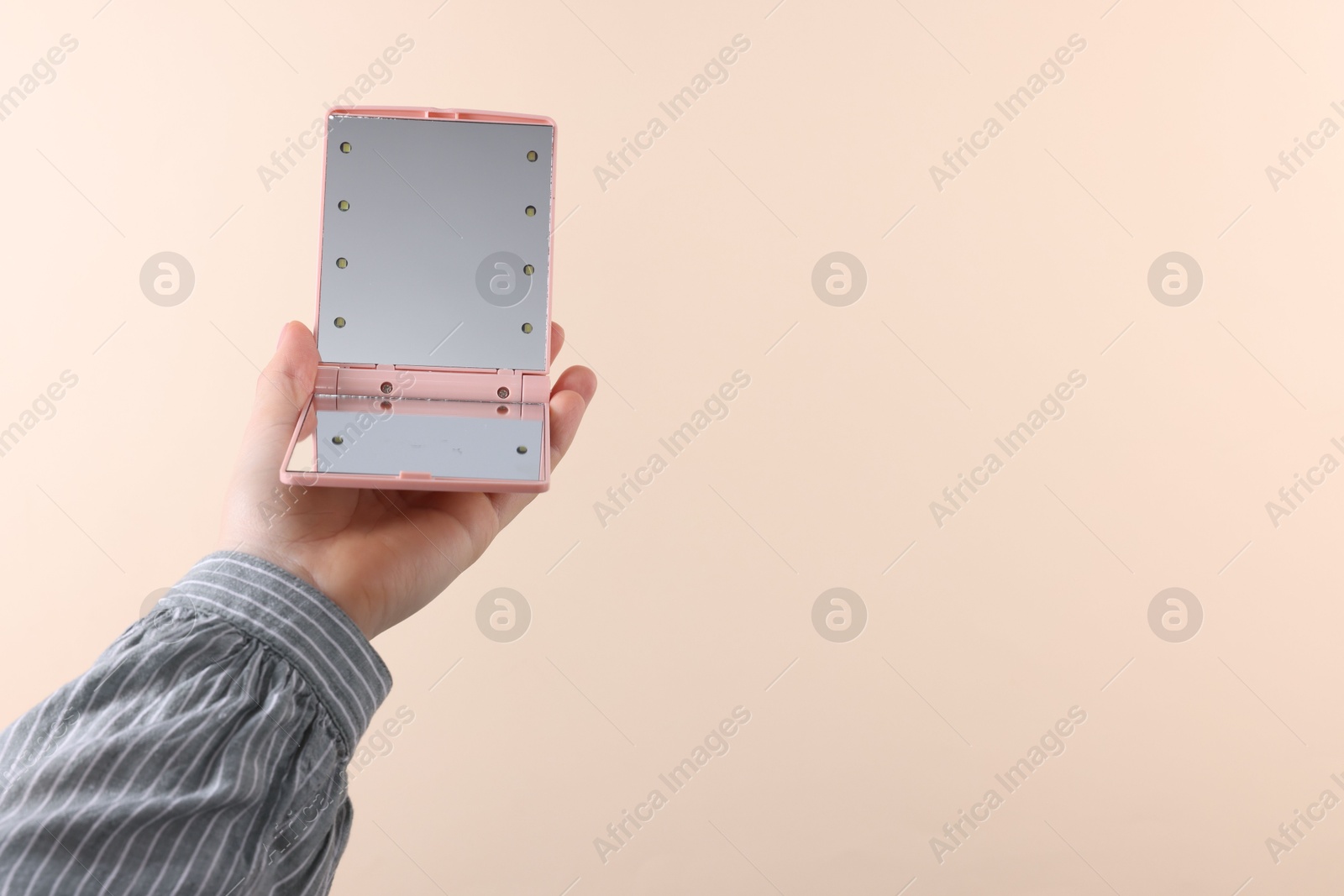 Photo of Woman holding pocket mirror on beige background, closeup. Space for text