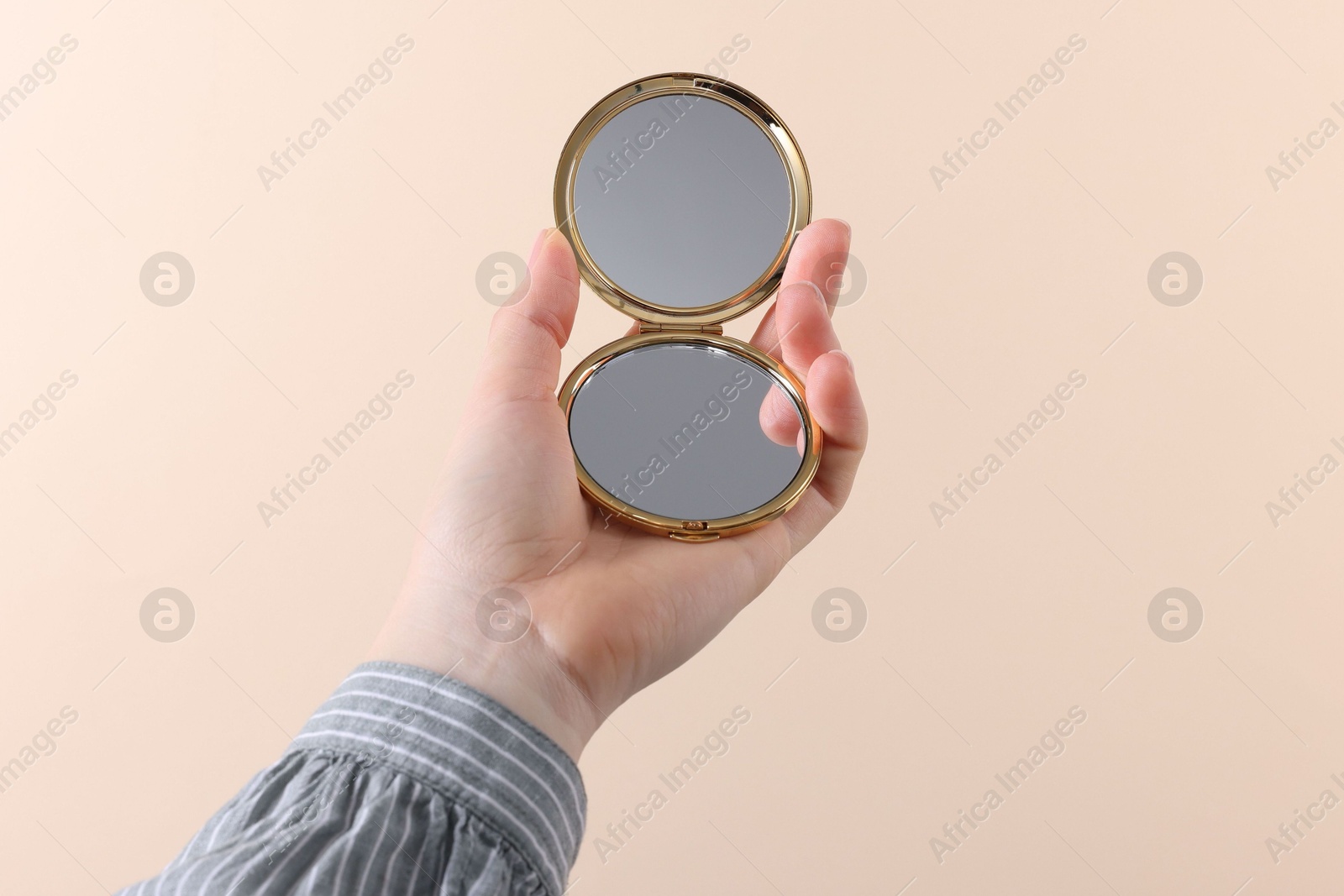 Photo of Woman holding pocket mirror on beige background, closeup