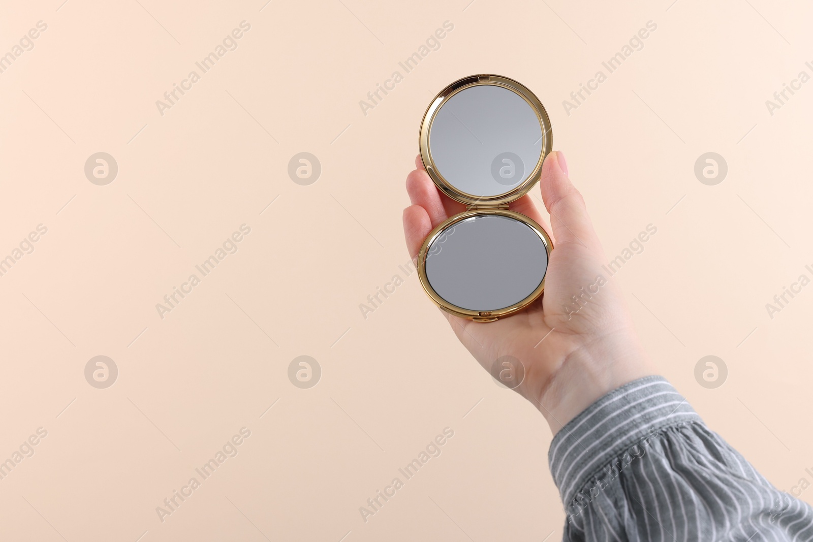 Photo of Woman holding pocket mirror on beige background, closeup. Space for text