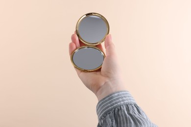 Woman holding pocket mirror on beige background, closeup