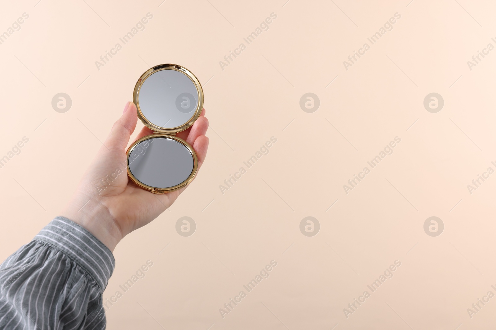 Photo of Woman holding pocket mirror on beige background, closeup. Space for text