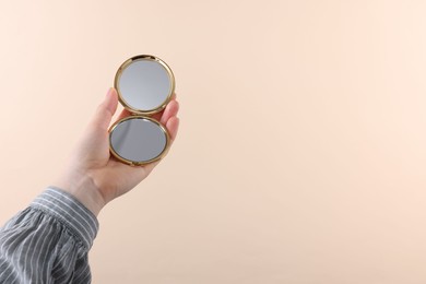 Woman holding pocket mirror on beige background, closeup. Space for text