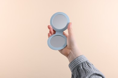 Woman holding pocket mirror on beige background, closeup