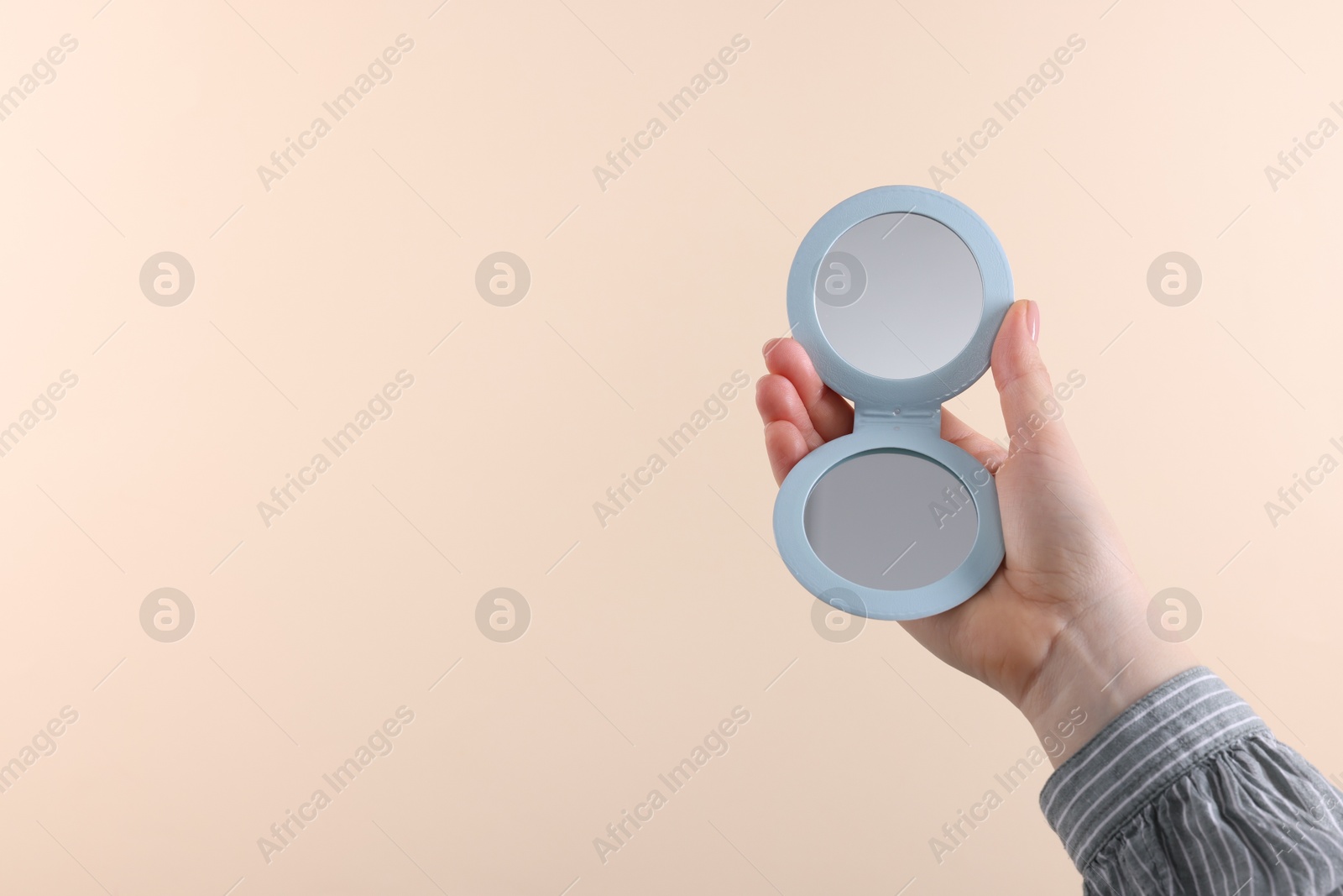 Photo of Woman holding pocket mirror on beige background, closeup. Space for text