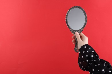 Photo of Woman holding beautiful mirror on red background, closeup. Space for text