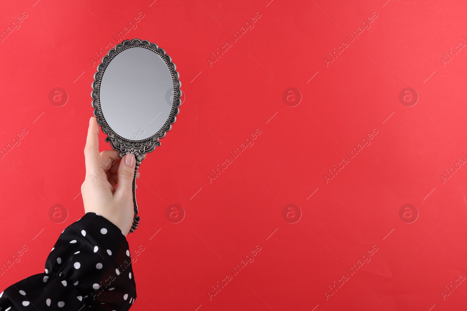 Photo of Woman holding beautiful mirror on red background, closeup. Space for text