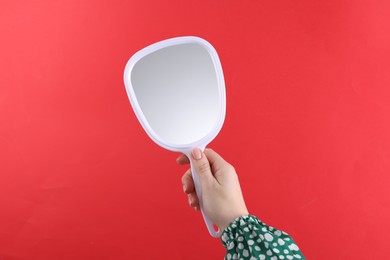 Photo of Woman holding handheld mirror on red background, closeup