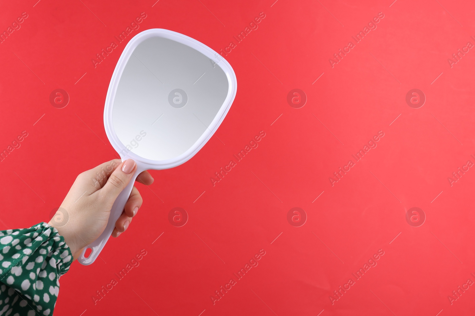 Photo of Woman holding handheld mirror on red background, closeup. Space for text