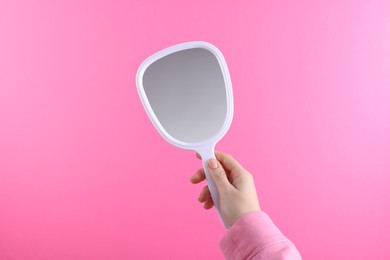 Woman holding handheld mirror on pink background, closeup