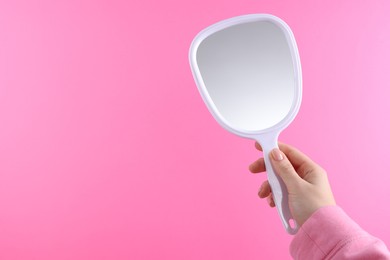 Photo of Woman holding handheld mirror on pink background, closeup. Space for text