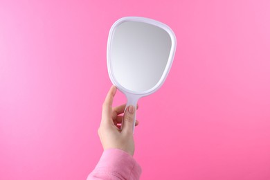 Photo of Woman holding handheld mirror on pink background, closeup