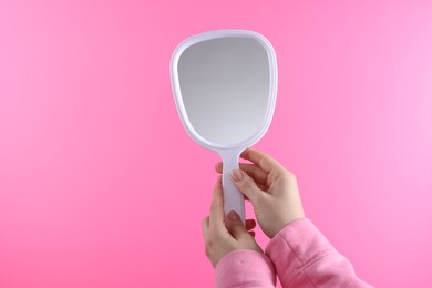 Photo of Woman holding handheld mirror on pink background, closeup. Space for text