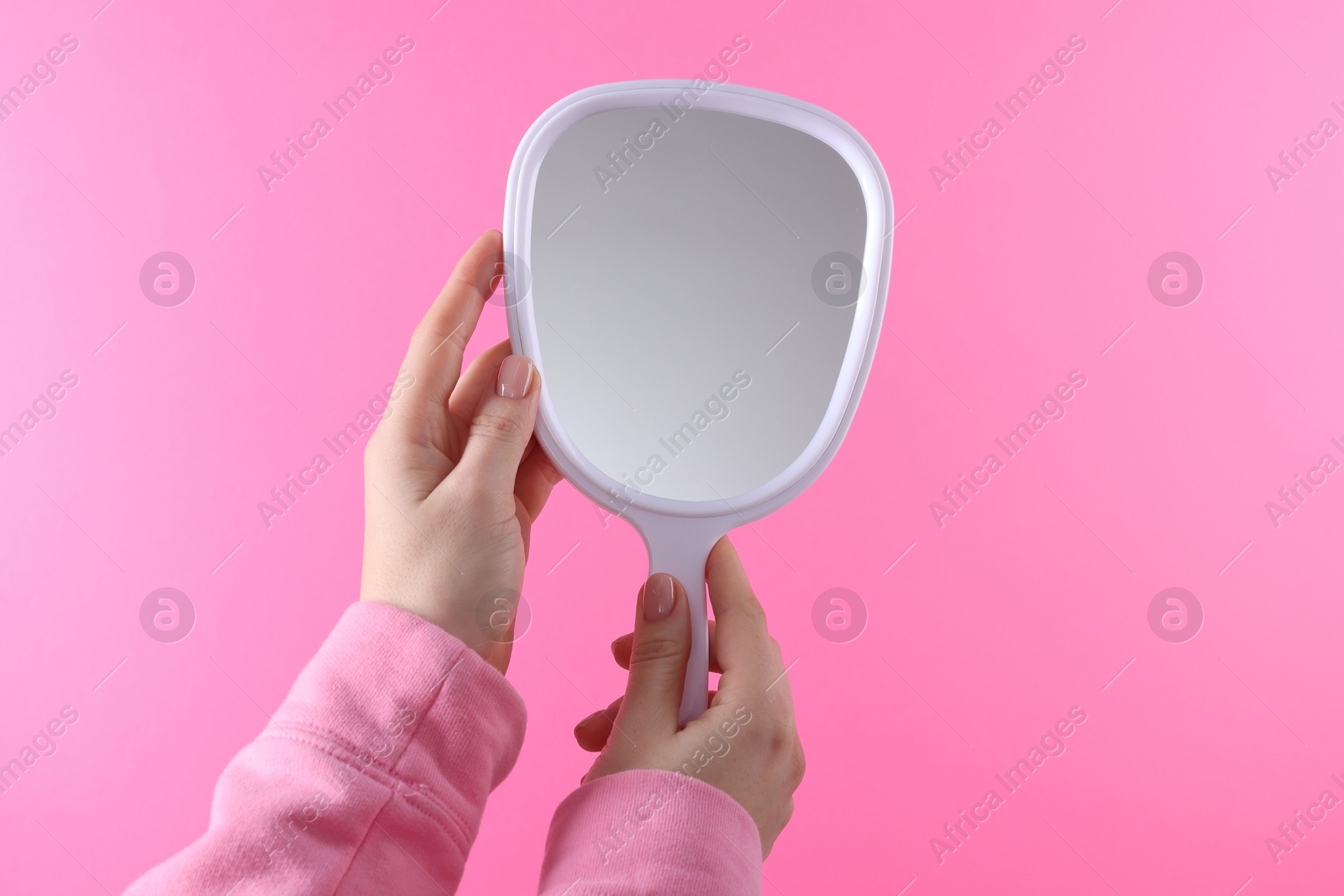 Photo of Woman holding handheld mirror on pink background, closeup