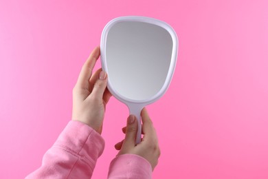 Woman holding handheld mirror on pink background, closeup