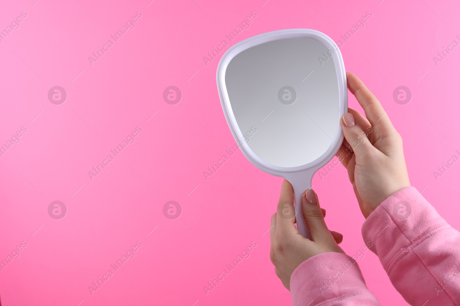 Photo of Woman holding handheld mirror on pink background, closeup. Space for text