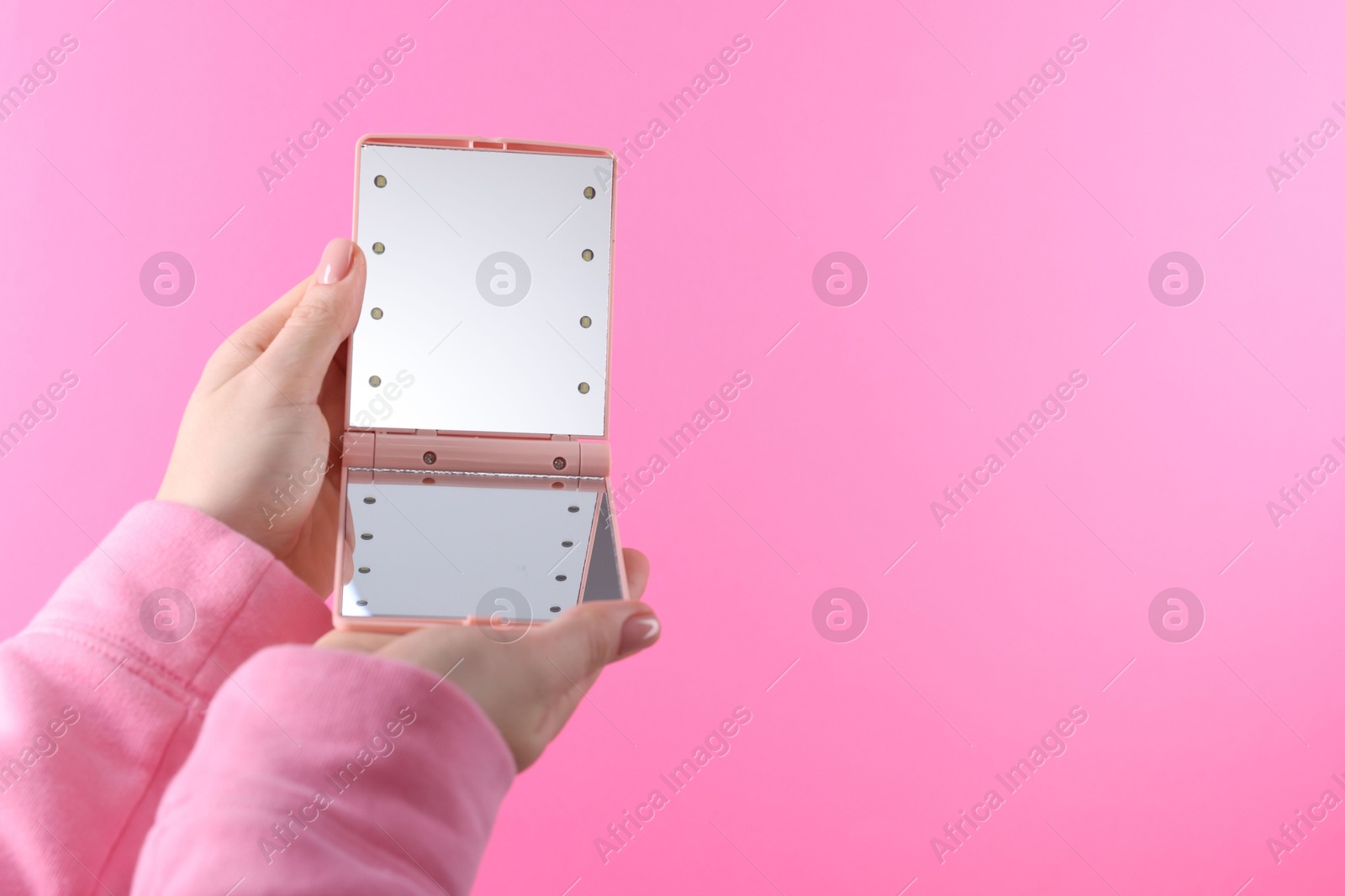 Photo of Woman holding pocket mirror on pink background, closeup. Space for text