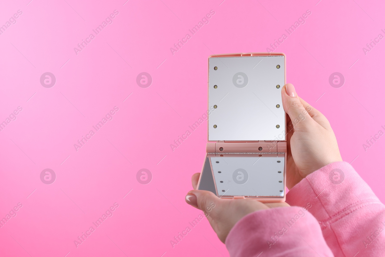 Photo of Woman holding pocket mirror on pink background, closeup. Space for text