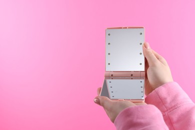 Photo of Woman holding pocket mirror on pink background, closeup. Space for text