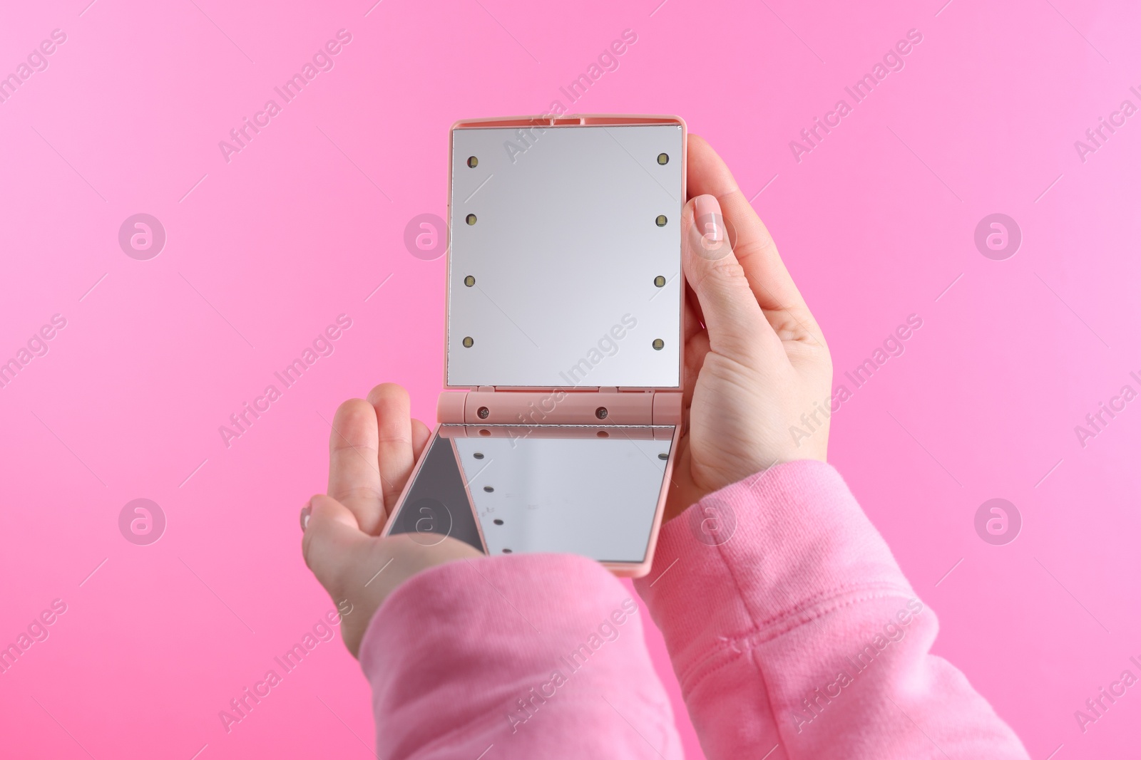 Photo of Woman holding pocket mirror on pink background, closeup