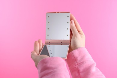 Woman holding pocket mirror on pink background, closeup