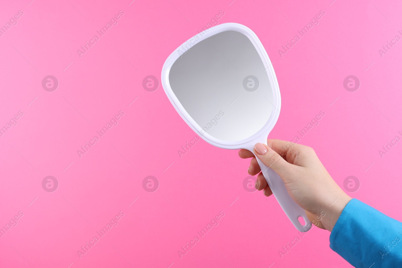 Photo of Woman holding handheld mirror on pink background, closeup. Space for text