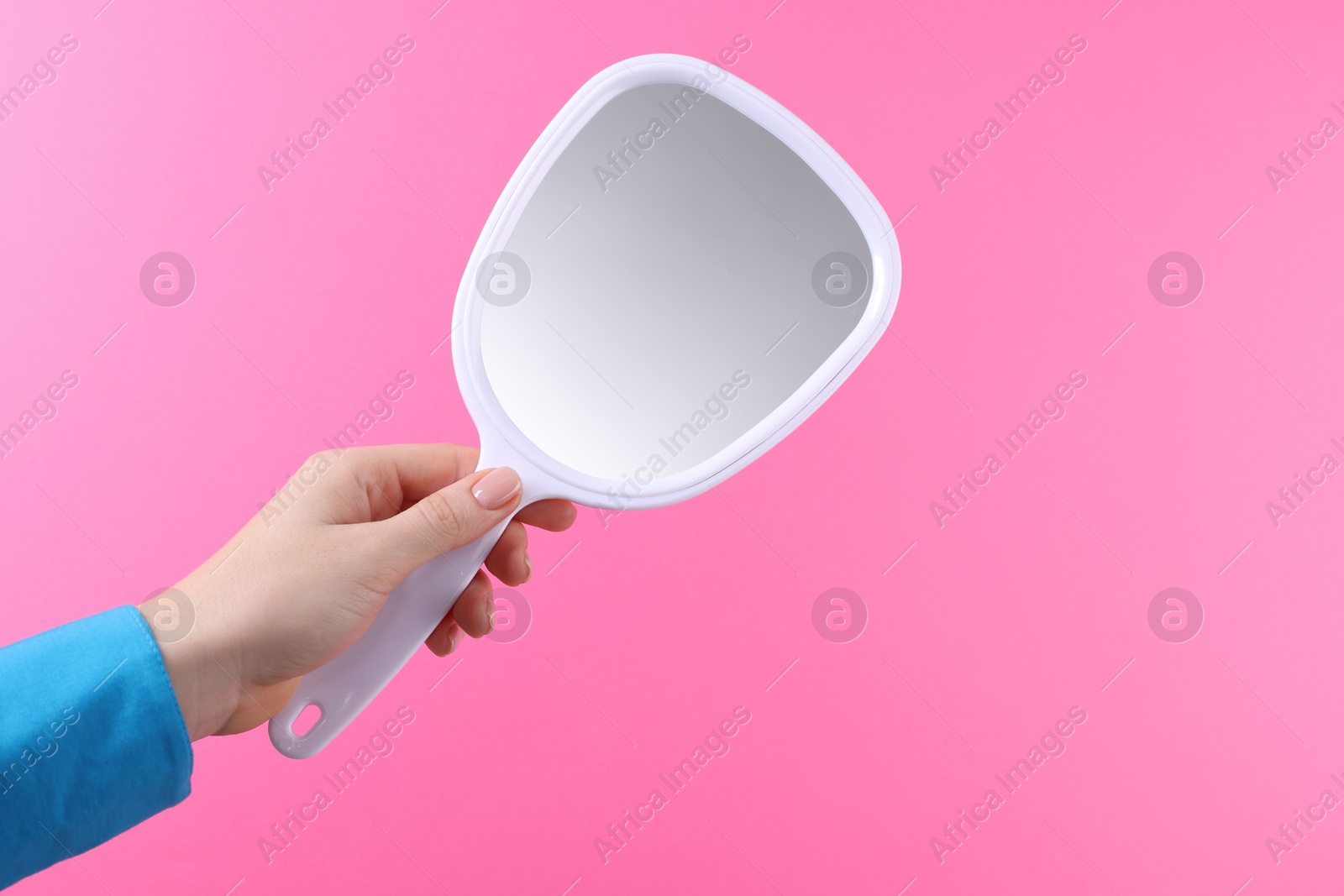 Photo of Woman holding handheld mirror on pink background, closeup. Space for text