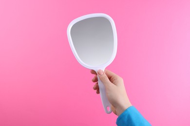 Woman holding handheld mirror on pink background, closeup