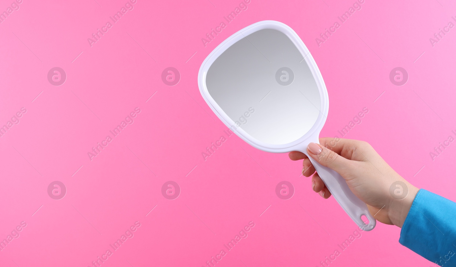 Photo of Woman holding handheld mirror on pink background, closeup. Space for text