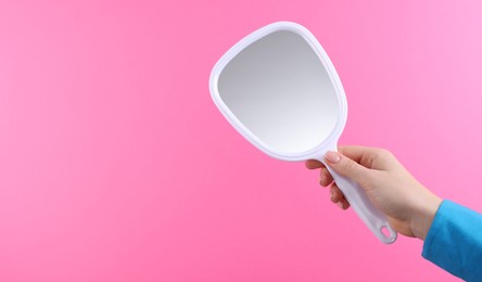 Photo of Woman holding handheld mirror on pink background, closeup. Space for text