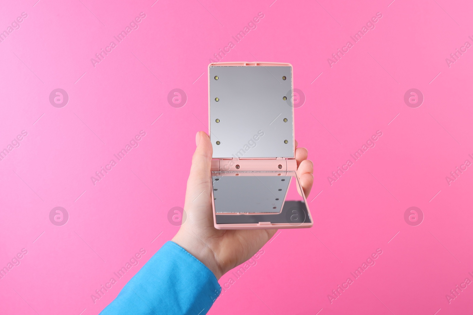 Photo of Woman holding pocket mirror on pink background, closeup