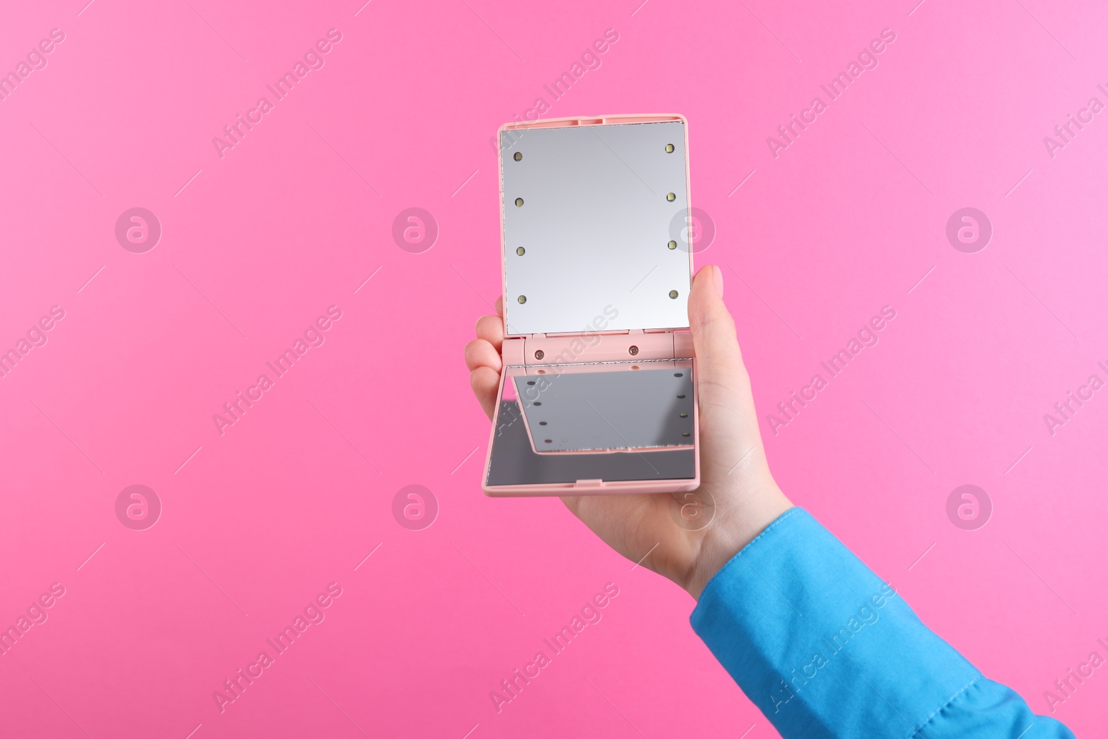 Photo of Woman holding pocket mirror on pink background, closeup. Space for text