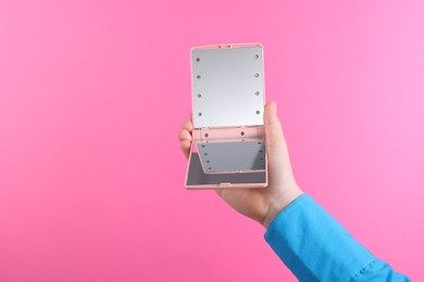 Woman holding pocket mirror on pink background, closeup. Space for text