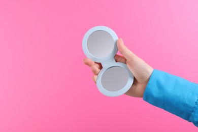 Photo of Woman holding pocket mirror on pink background, closeup. Space for text