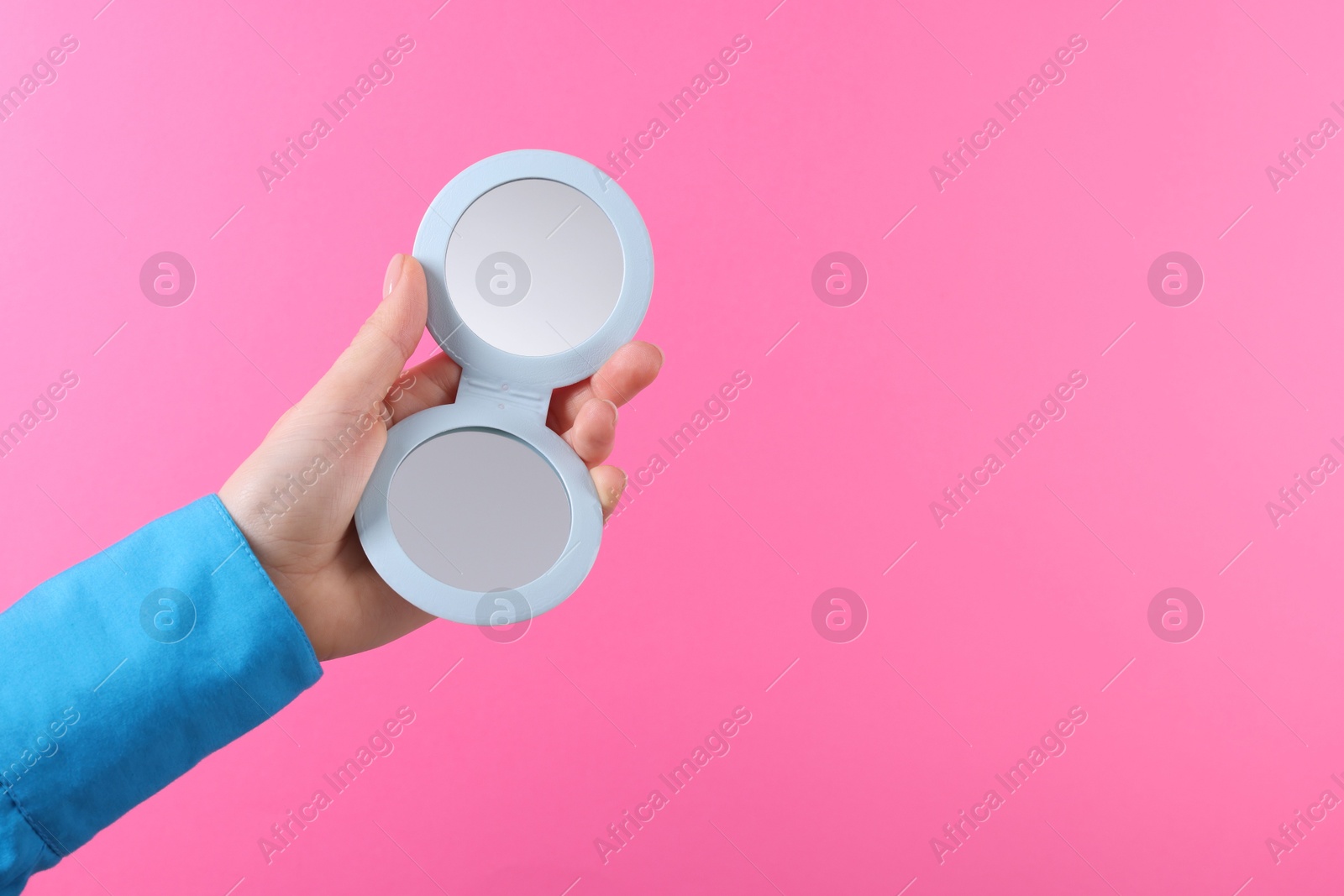 Photo of Woman holding pocket mirror on pink background, closeup. Space for text