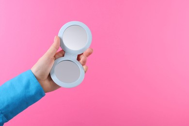 Woman holding pocket mirror on pink background, closeup. Space for text