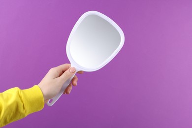 Photo of Woman holding handheld mirror on violet background, closeup. Space for text